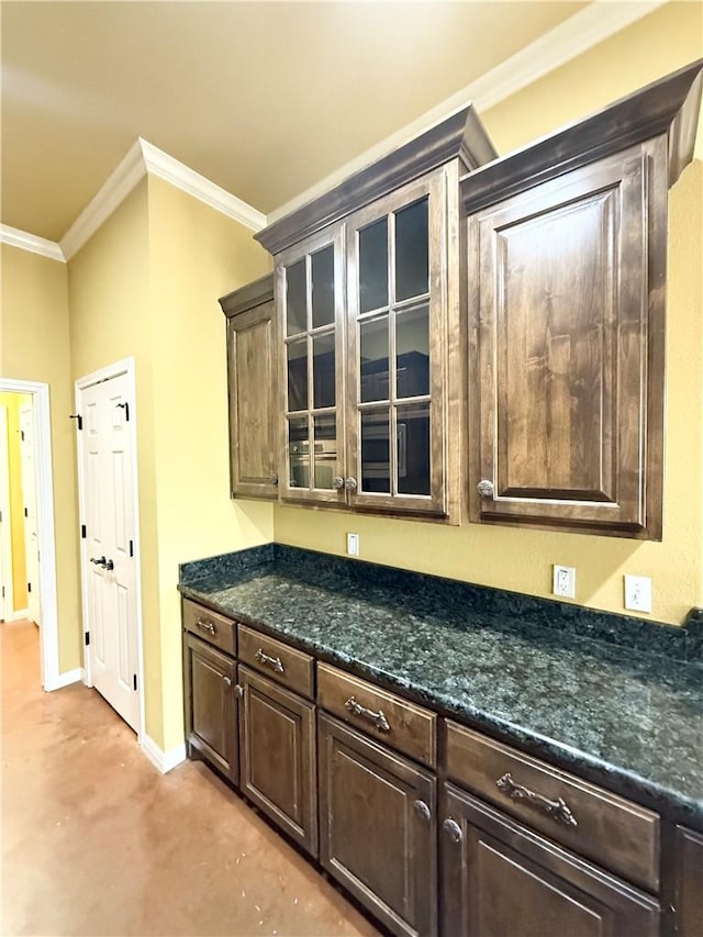kitchen featuring dark brown cabinets, glass insert cabinets, baseboards, dark stone counters, and ornamental molding