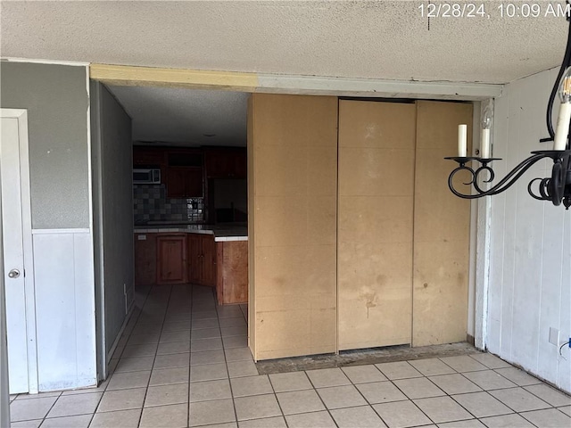 interior space featuring stainless steel microwave, a wainscoted wall, light tile patterned floors, decorative backsplash, and a textured ceiling