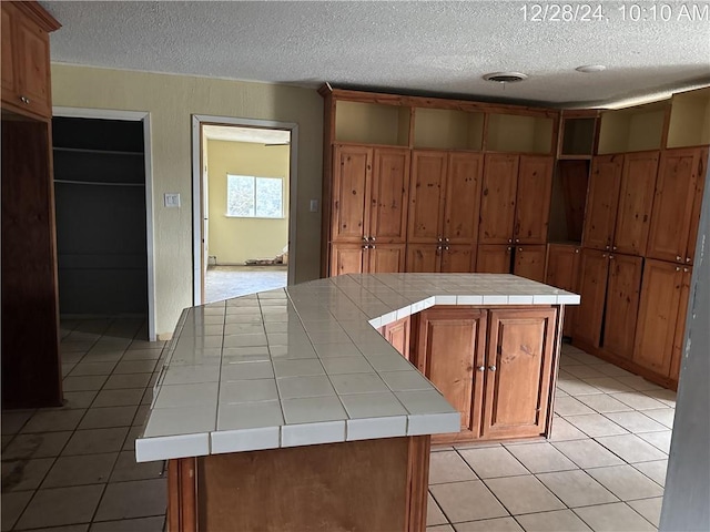 kitchen featuring light tile patterned floors, tile counters, a textured ceiling, brown cabinets, and a center island