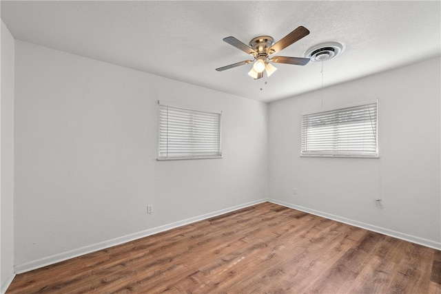 empty room featuring visible vents, wood finished floors, baseboards, and ceiling fan