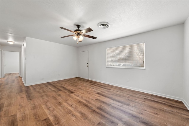 unfurnished room with wood finished floors, baseboards, a ceiling fan, visible vents, and a textured ceiling