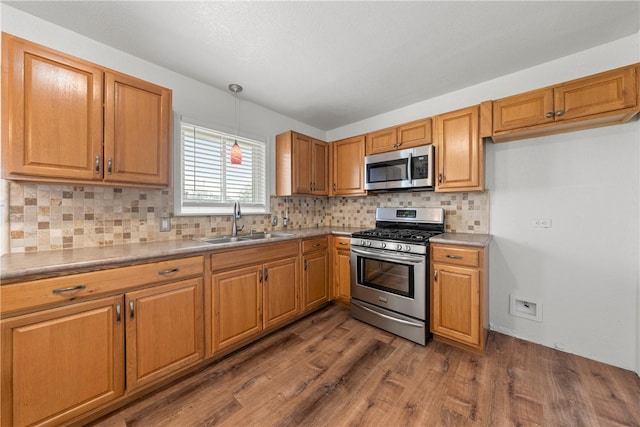 kitchen with dark wood-type flooring, pendant lighting, a sink, stainless steel appliances, and decorative backsplash