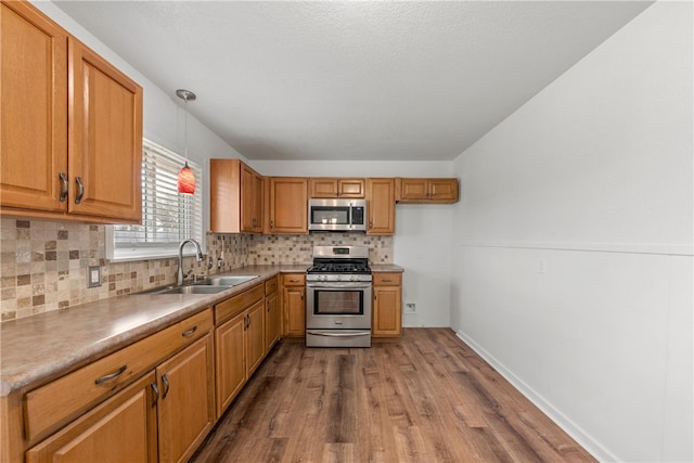 kitchen featuring tasteful backsplash, wood finished floors, hanging light fixtures, stainless steel appliances, and a sink