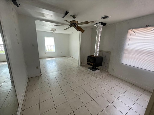 unfurnished living room with visible vents, a ceiling fan, light tile patterned flooring, baseboards, and a wood stove