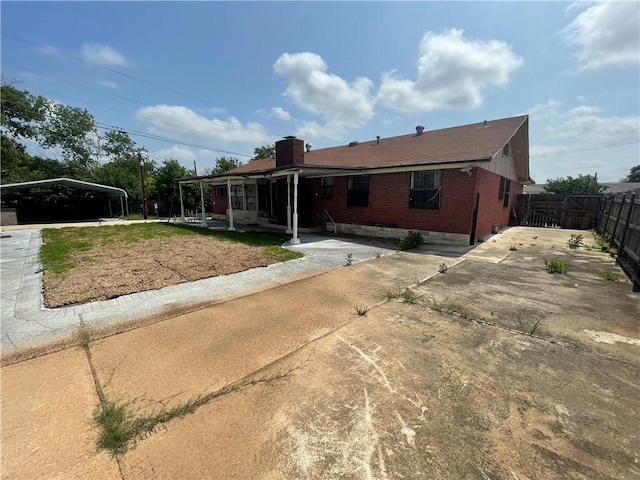 view of front facade featuring fence, driveway, a chimney, a carport, and brick siding