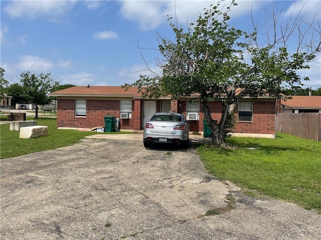 ranch-style home featuring a front yard, fence, brick siding, and driveway