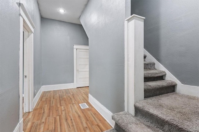 hall featuring wood finished floors, stairs, a textured wall, baseboards, and visible vents