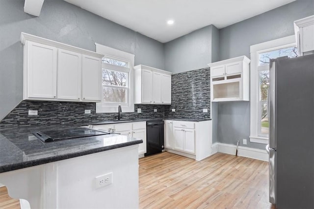kitchen featuring light wood finished floors, a sink, freestanding refrigerator, a peninsula, and tasteful backsplash