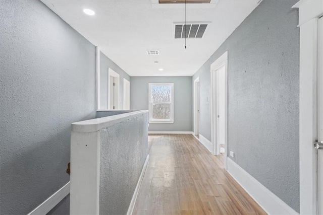 hall with wood finished floors, attic access, a textured wall, baseboards, and visible vents