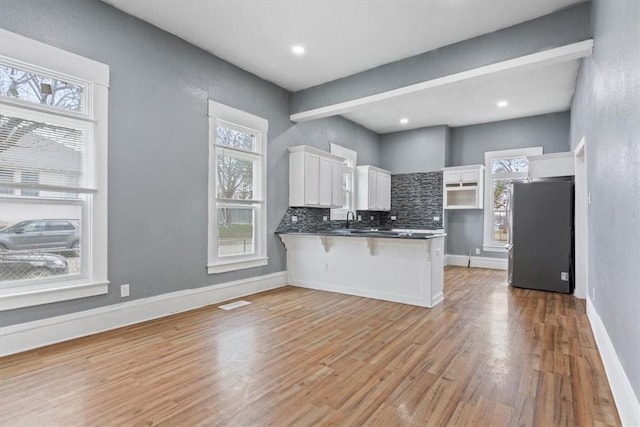 kitchen with light wood finished floors, a peninsula, a kitchen breakfast bar, freestanding refrigerator, and white cabinetry