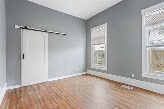 interior space featuring a barn door, baseboards, wood finished floors, and visible vents