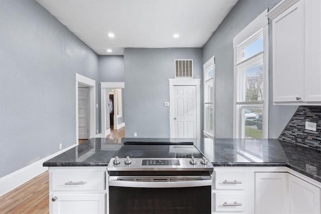 kitchen featuring light wood finished floors, dark stone countertops, white cabinetry, decorative backsplash, and stainless steel range with electric stovetop