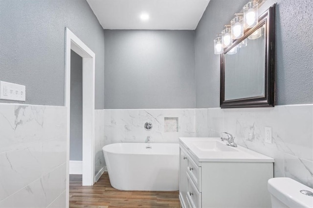 full bathroom with tile walls, a freestanding tub, vanity, and wood finished floors