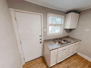 kitchen featuring white cabinetry, baseboards, light wood finished floors, and a sink