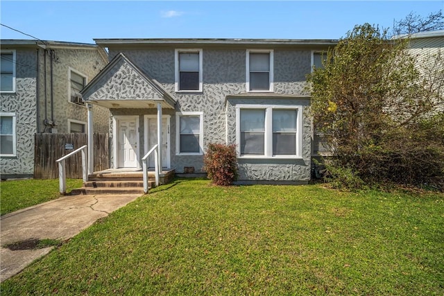 view of front of house featuring stucco siding, a front yard, and fence