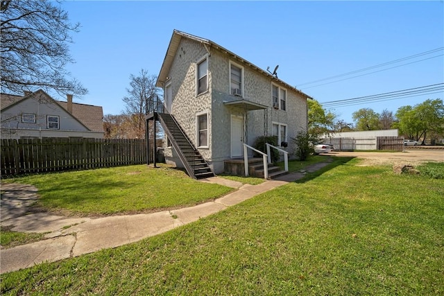 back of house with stucco siding, a lawn, and fence