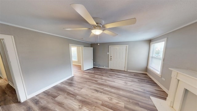 unfurnished living room featuring baseboards, ornamental molding, light wood-style flooring, a textured ceiling, and a ceiling fan