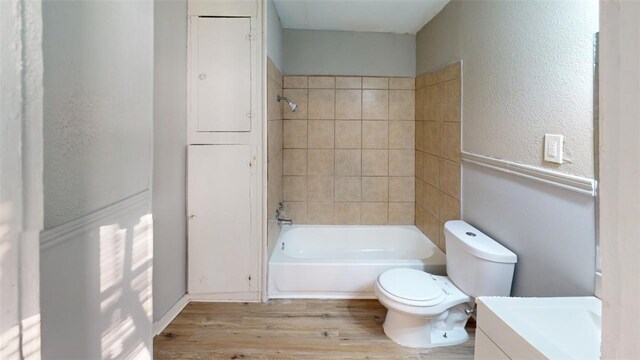 full bath featuring toilet, vanity, wood finished floors, a textured wall, and washtub / shower combination