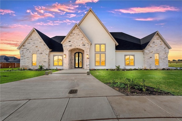 french country inspired facade with stone siding, stucco siding, french doors, and a front yard