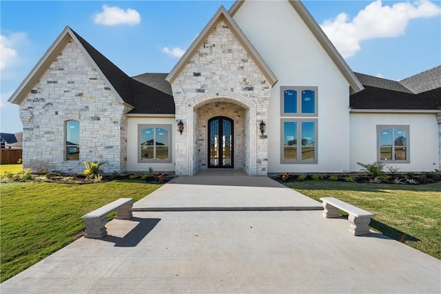 french country home featuring stone siding, french doors, a shingled roof, and a front lawn