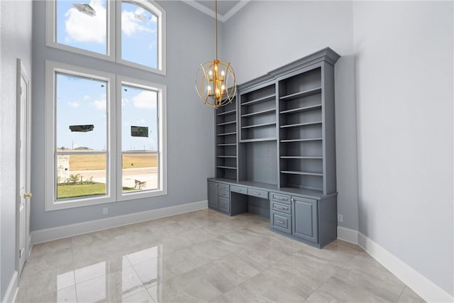 unfurnished office with ornamental molding, an inviting chandelier, baseboards, a towering ceiling, and built in study area