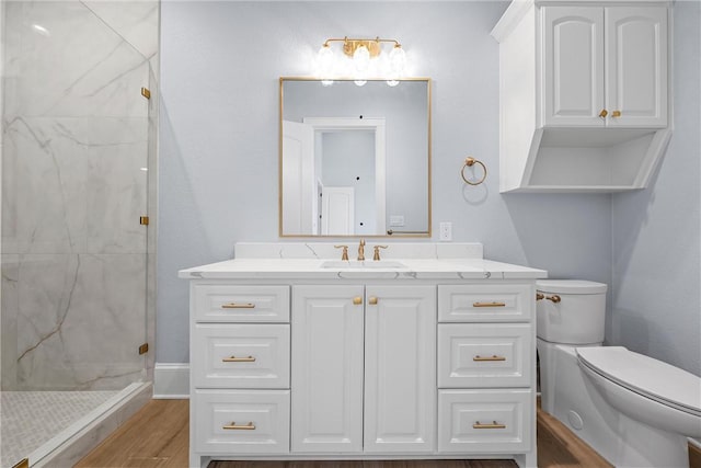 bathroom featuring a marble finish shower, toilet, wood finished floors, and vanity
