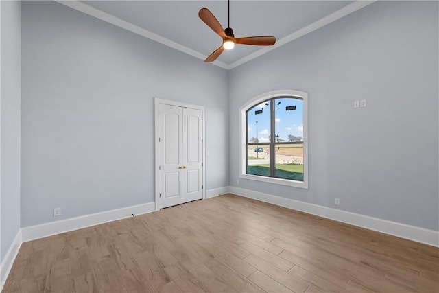 spare room with baseboards, ceiling fan, vaulted ceiling, light wood-style floors, and crown molding