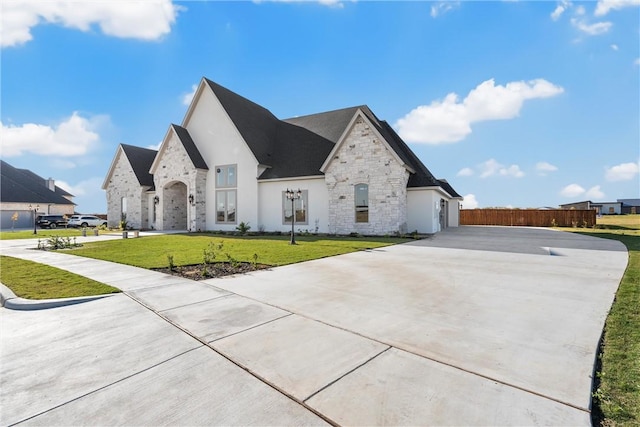 view of front of property with fence, concrete driveway, a front yard, stucco siding, and stone siding