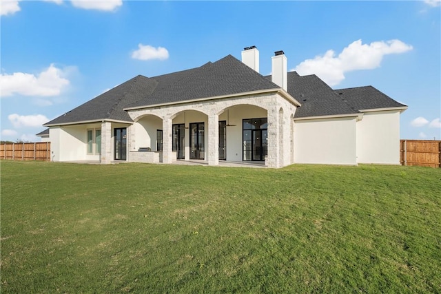 back of property featuring a shingled roof, fence, stucco siding, a chimney, and a yard