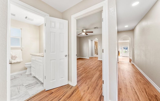 corridor with light wood-type flooring, visible vents, arched walkways, and baseboards