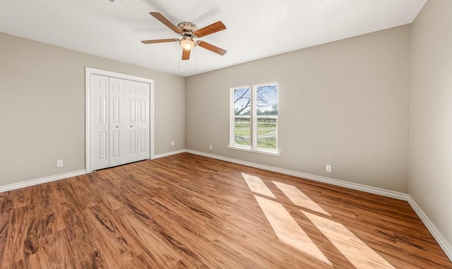 unfurnished bedroom featuring a closet, a ceiling fan, baseboards, and wood finished floors