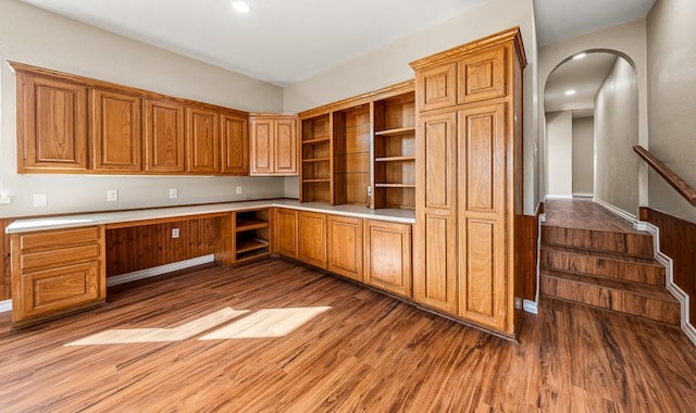 kitchen featuring open shelves, arched walkways, built in desk, and light wood finished floors