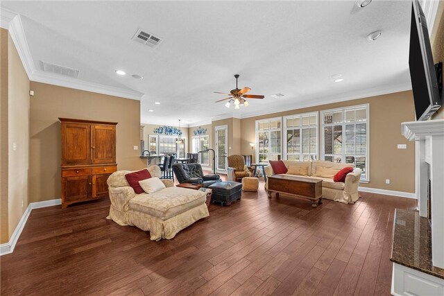 living area featuring a ceiling fan, baseboards, visible vents, ornamental molding, and dark wood-style flooring