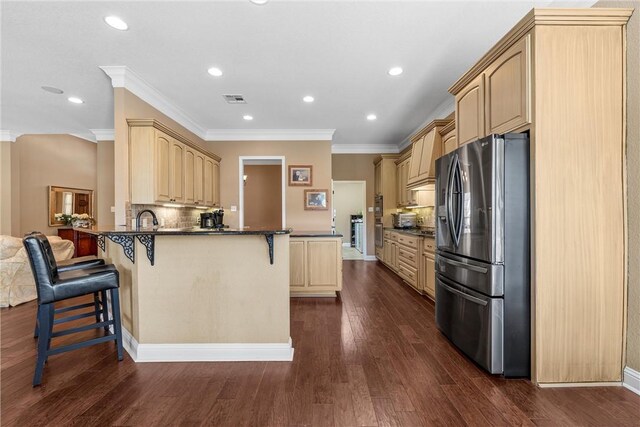 kitchen with stainless steel fridge, a peninsula, a kitchen bar, dark countertops, and light brown cabinetry