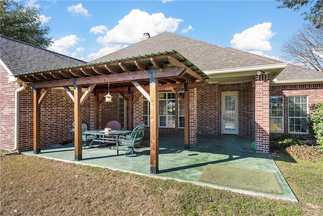 back of house featuring a lawn, a patio area, brick siding, and roof with shingles