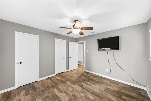 unfurnished bedroom with ceiling fan, two closets, baseboards, wood finished floors, and visible vents