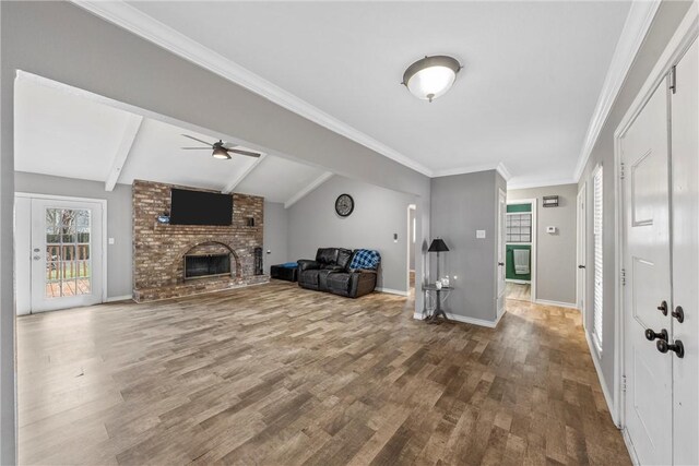 living room featuring a brick fireplace, wood finished floors, baseboards, ceiling fan, and vaulted ceiling with beams
