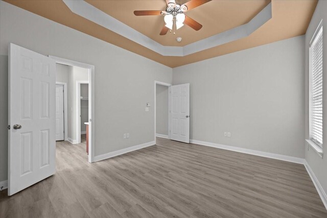 187 Ashland Dr, Woodway, TX 76712 - unfurnished bedroom featuring baseboards, multiple windows, a tray ceiling, and wood finished floors