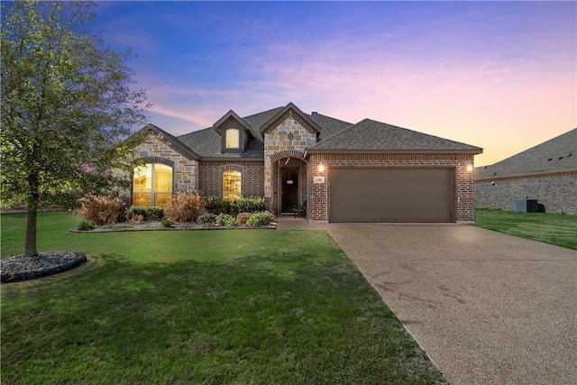 french country home featuring brick siding, a shingled roof, a front yard, a garage, and driveway