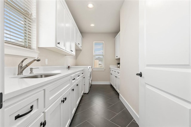 laundry area with baseboards, independent washer and dryer, cabinet space, a sink, and dark tile patterned flooring