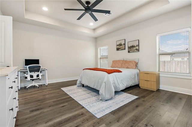 bedroom featuring dark wood-style floors, visible vents, baseboards, and a raised ceiling