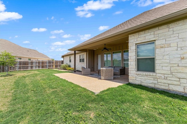 rear view of house featuring stone siding, ceiling fan, fence, and a yard