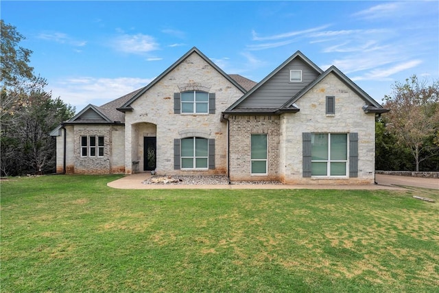 french provincial home featuring stone siding, a front lawn, and a shingled roof