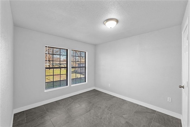 unfurnished room with a textured ceiling, baseboards, and dark tile patterned flooring