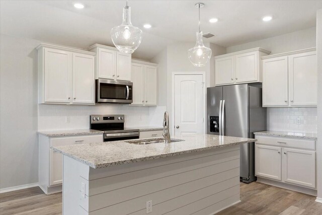 kitchen with a sink, appliances with stainless steel finishes, backsplash, white cabinets, and light wood-style floors
