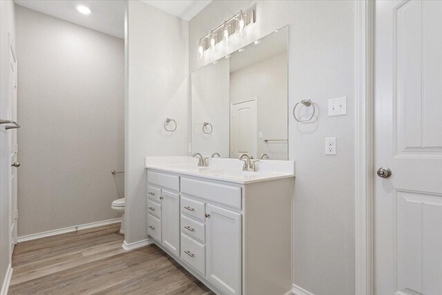 bathroom featuring baseboards, a sink, wood finished floors, and toilet