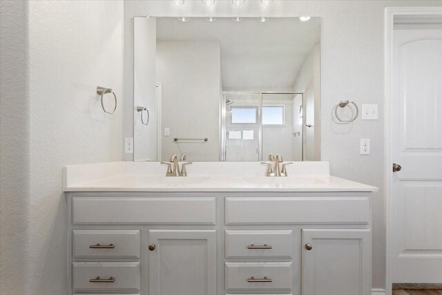 bathroom with double vanity, a shower with door, and a sink