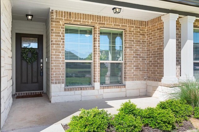 view of exterior entry with brick siding and a porch