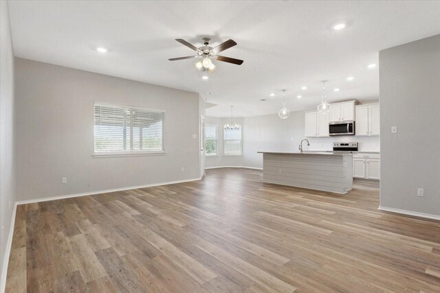 unfurnished living room with ceiling fan with notable chandelier, a sink, baseboards, light wood-style floors, and recessed lighting