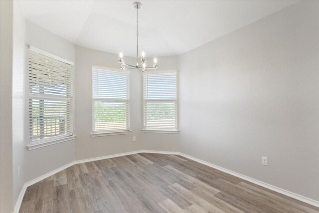 unfurnished dining area featuring a notable chandelier, baseboards, and wood finished floors